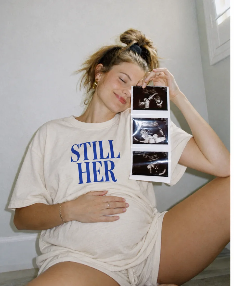 Expectant mother holding ultrasound photos in a STILL HER tee